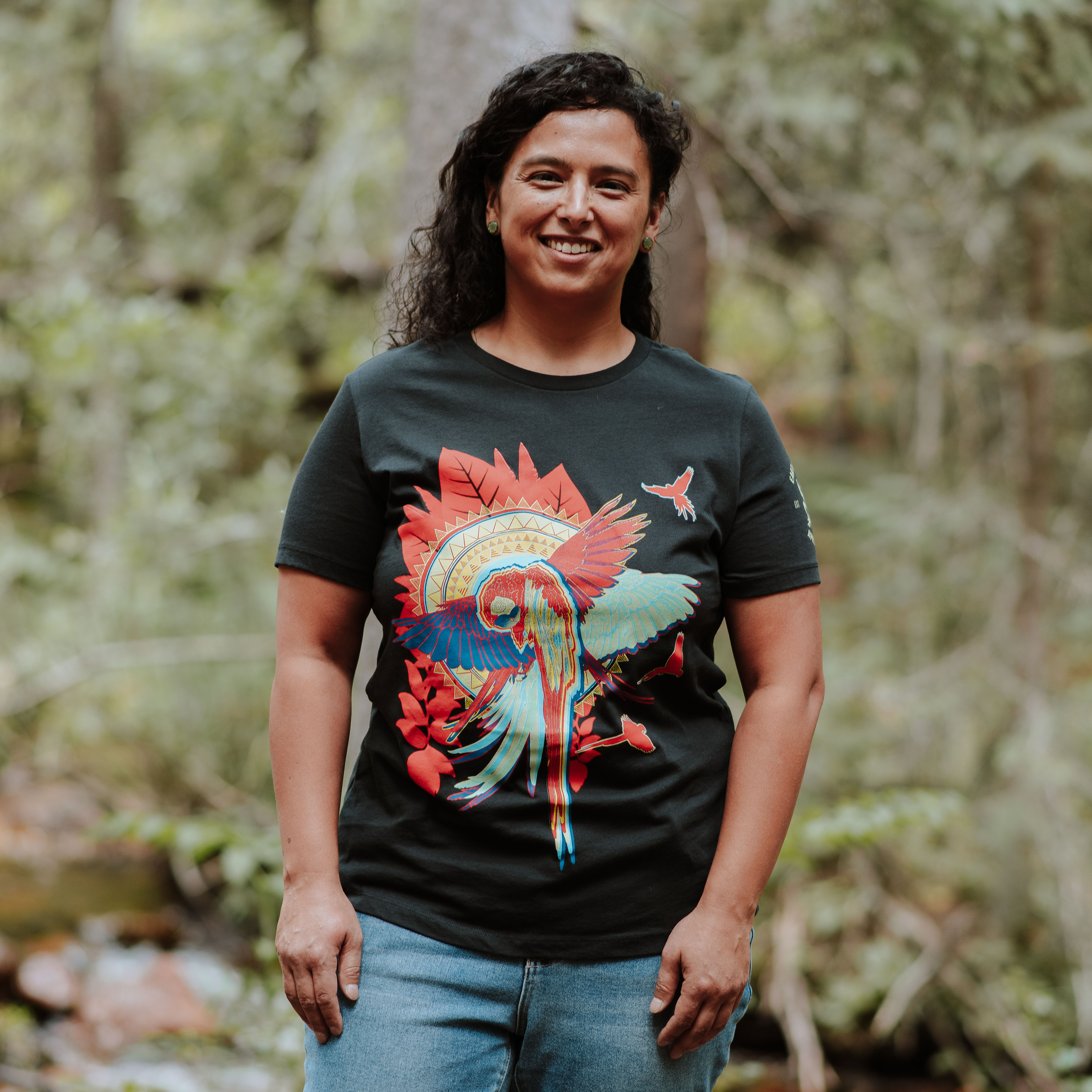 Woman wearing a black t-shirt with a colorful parrot design in a forest setting
