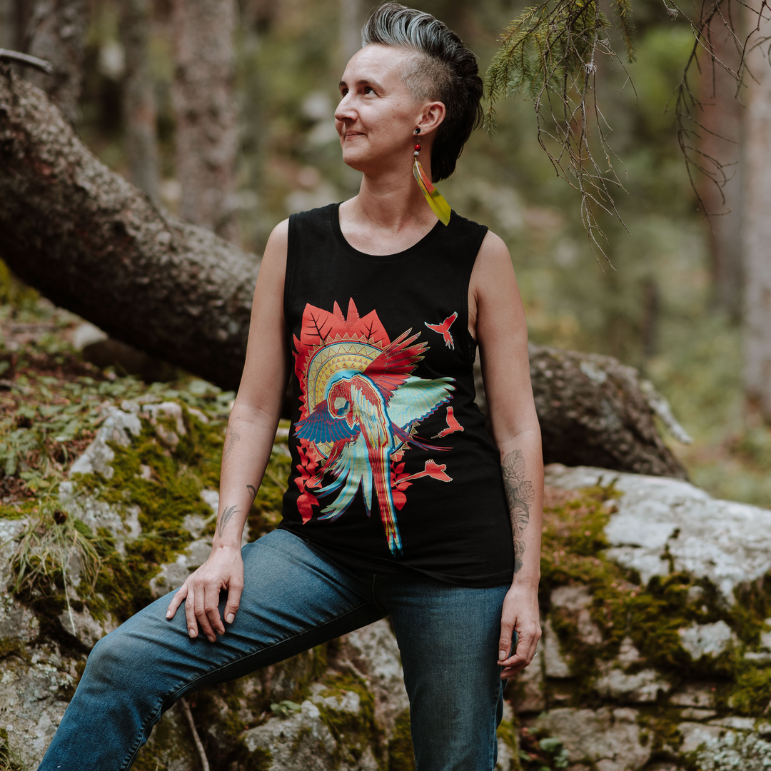 Woman wearing a black muscle tank with a colorful macaw design, sitting on a rock in a forest.