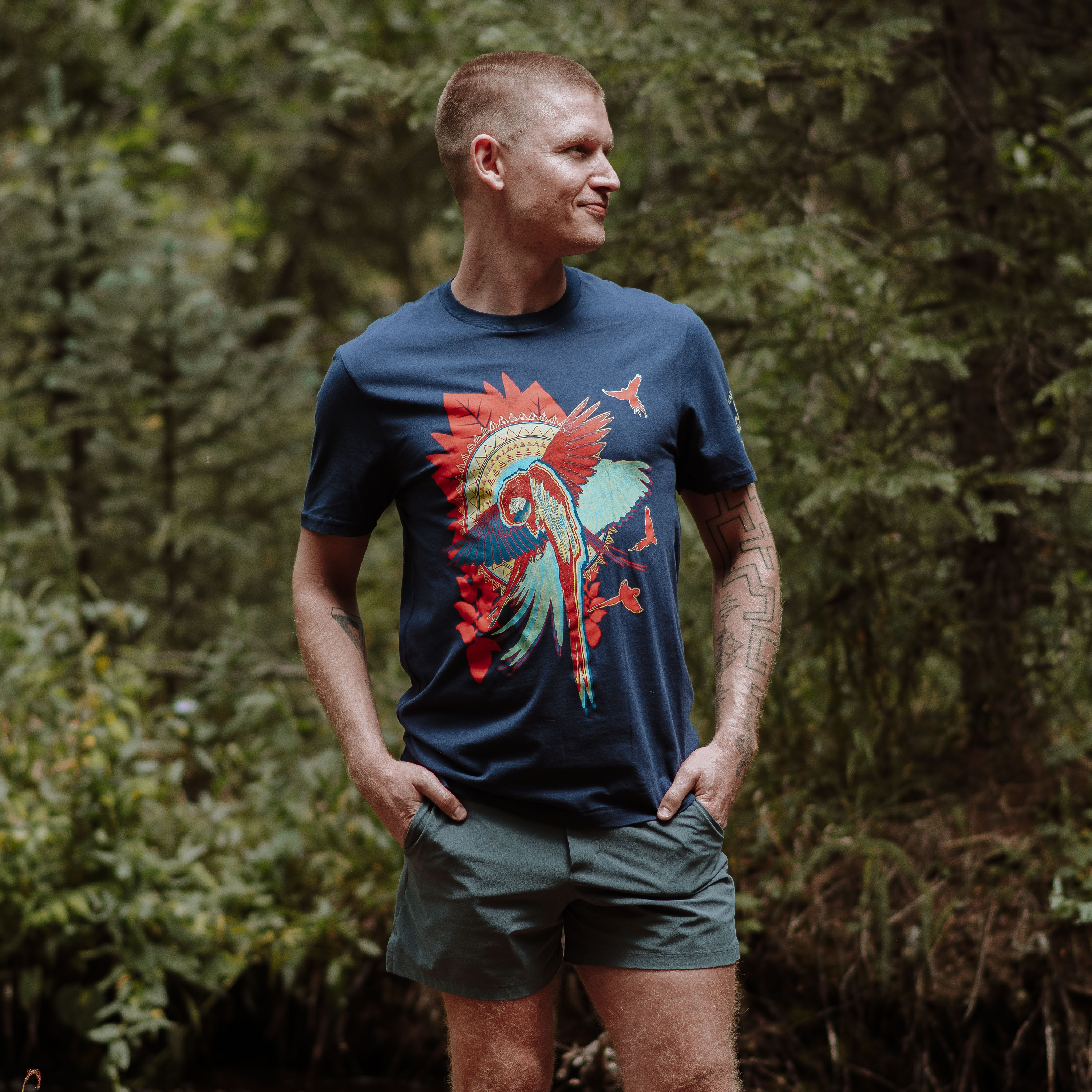 Man wearing a blue t-shirt with a colorful graphic design in a forest setting