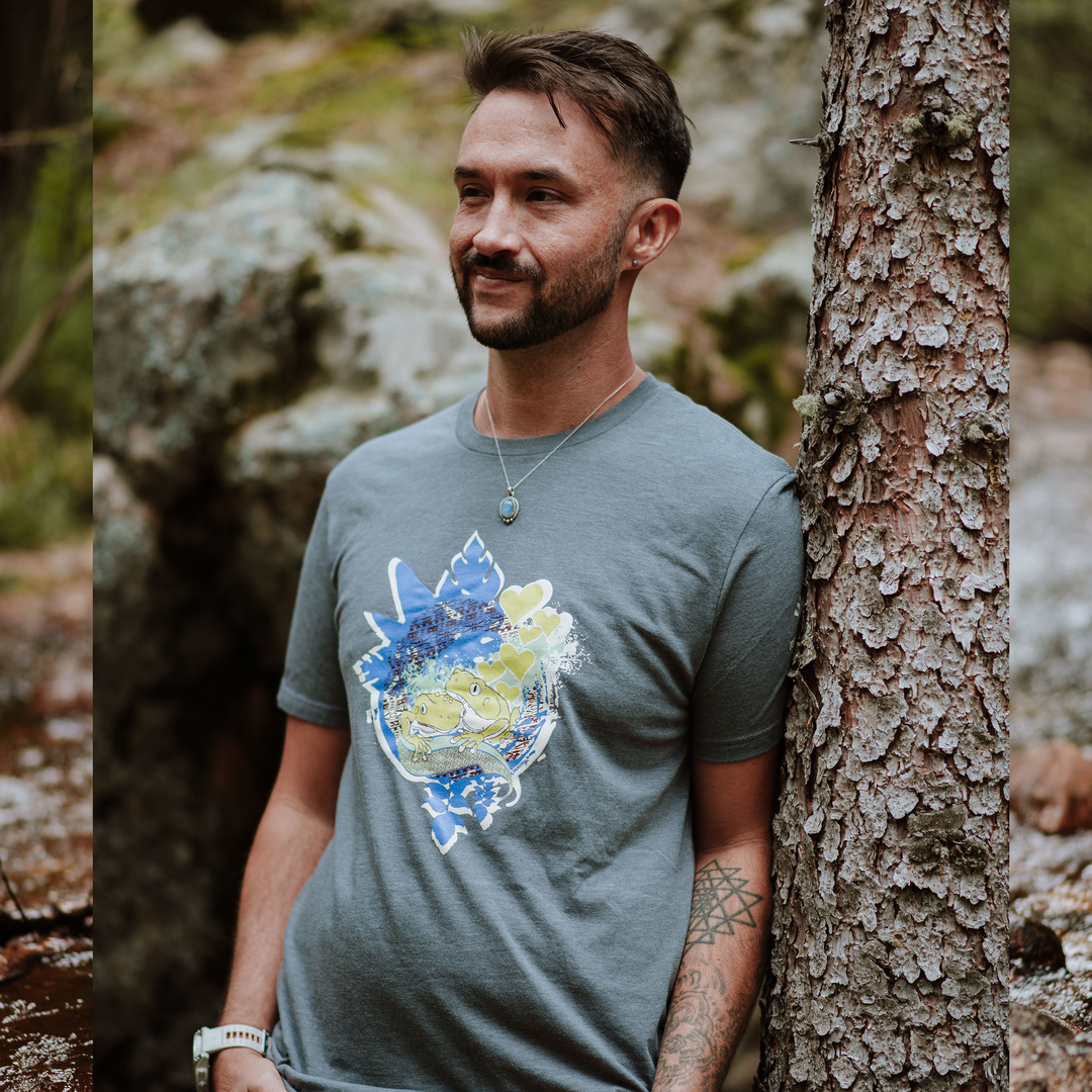 Man wearing a gray t-shirt with a colorful graphic design, standing next to a tree in a natural setting.