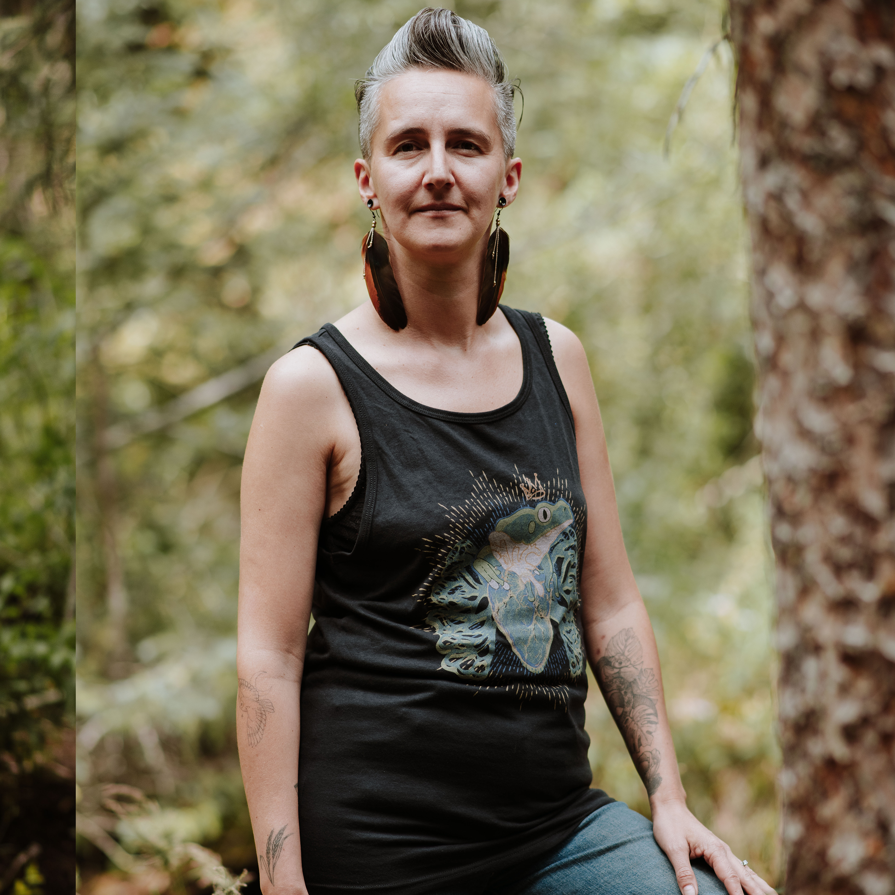 Person wearing a black tank top with a frog design in a forest setting