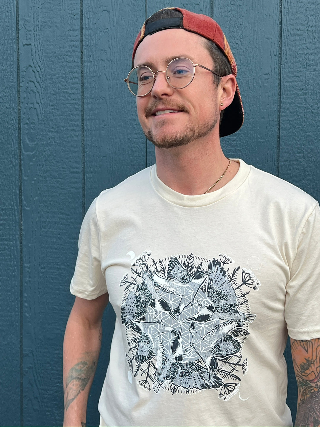 Man wearing a white t-shirt with a black and white graphic design against a blue wall.
