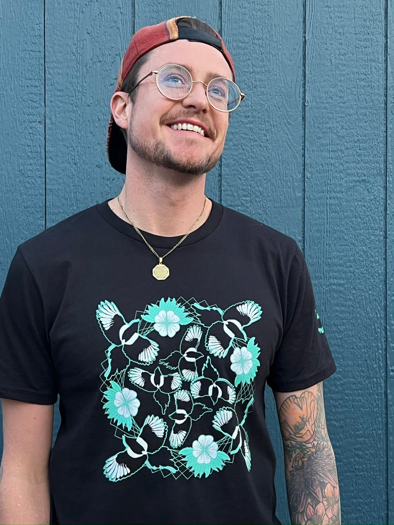 Man wearing a black t-shirt with a floral bird design, standing against a blue wall.