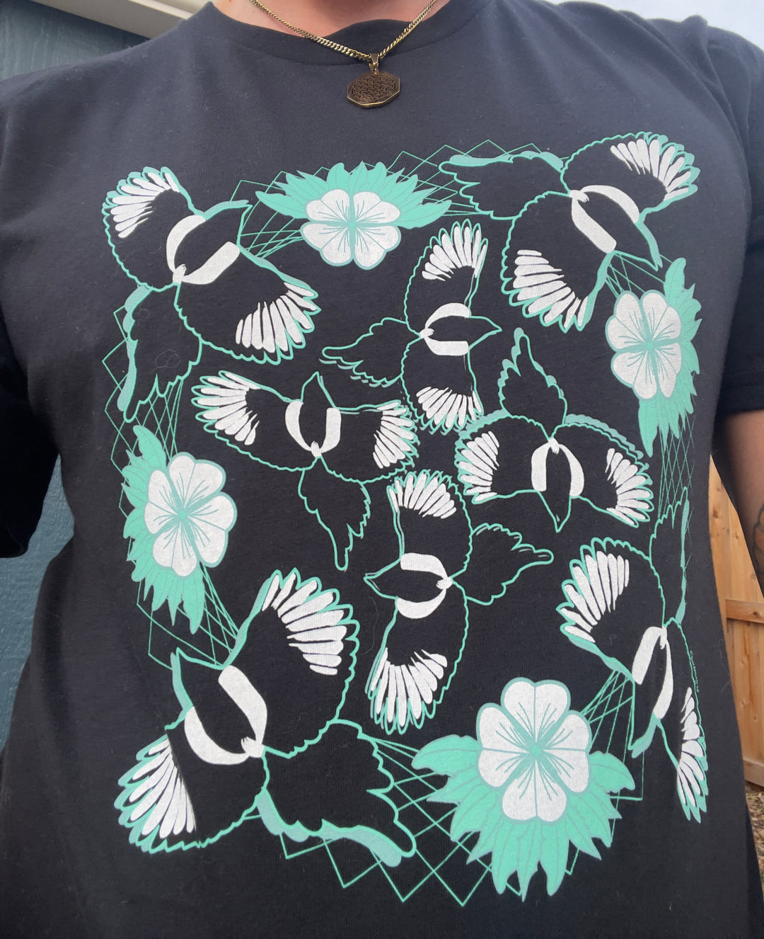 Black t-shirt with white and green floral and bird pattern worn by a person.