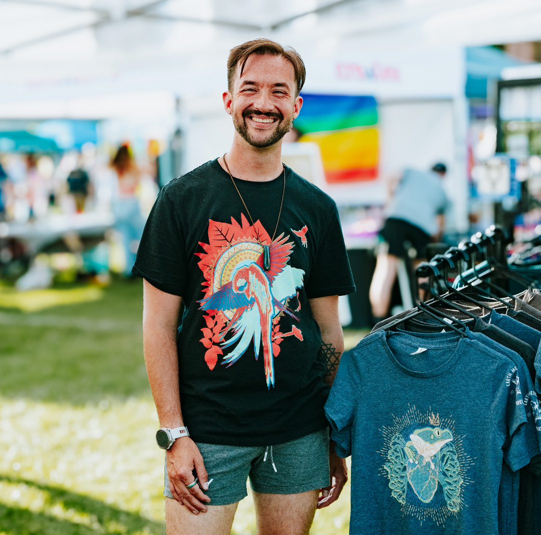 Man wearing a black t-shirt with a colorful graphic design at an outdoor event.