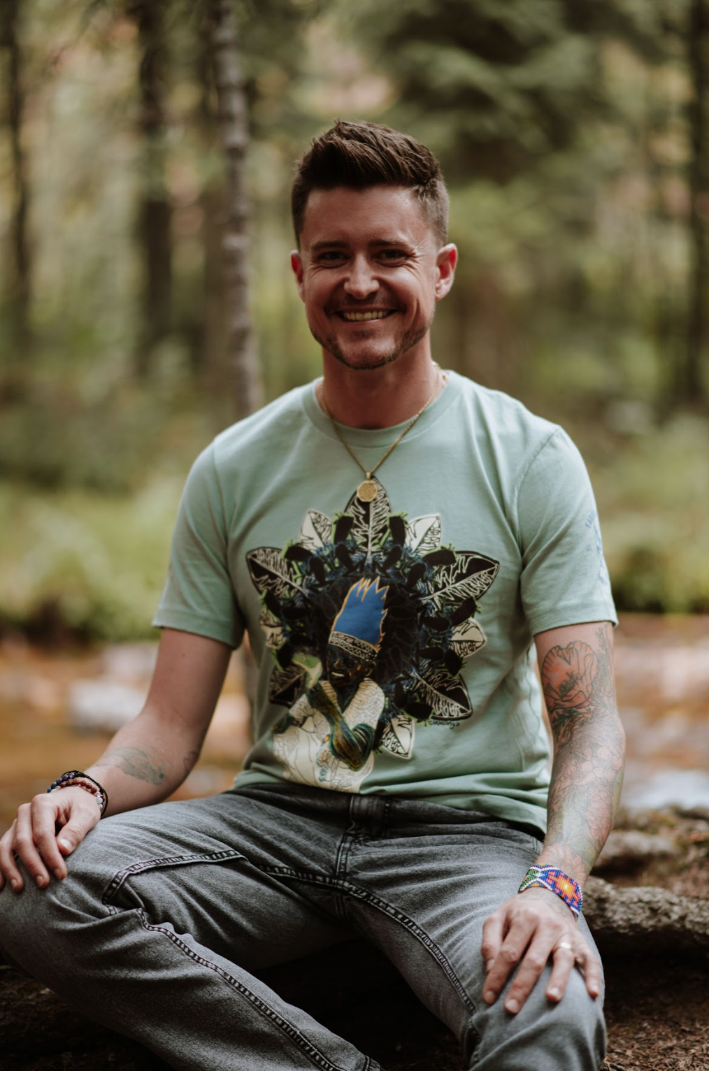 Man sitting in a forest wearing a light green t-shirt with a graphic design.