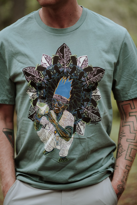 Person wearing a green t-shirt with a unique design of a Peruvian man, frog, and leaves.