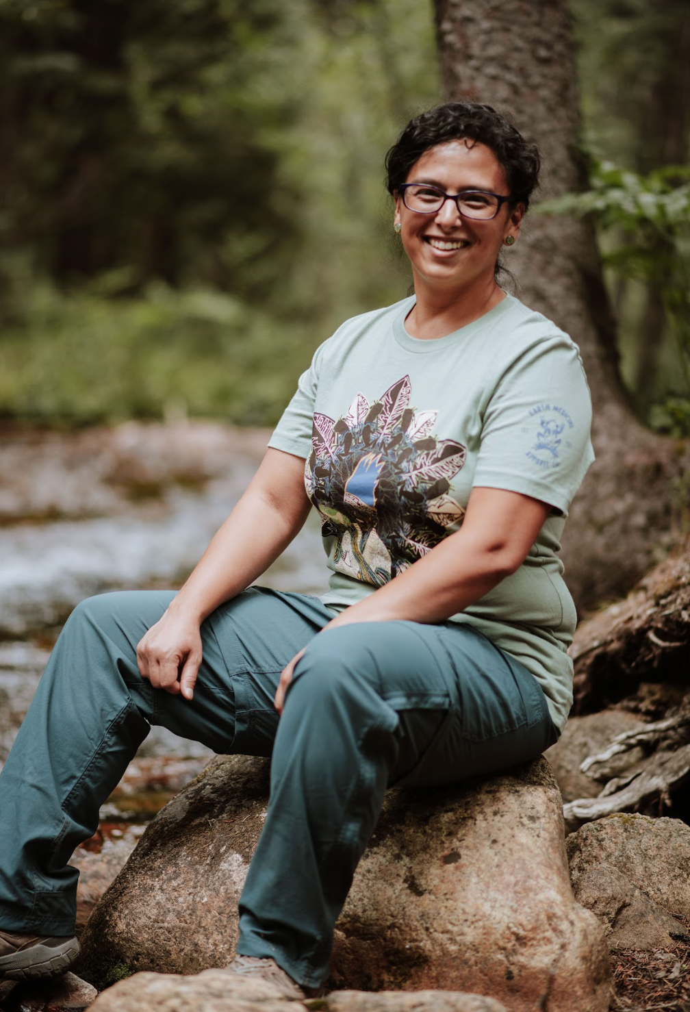 Woman sitting on a rock in a forest wearing a nature-themed t-shirt
